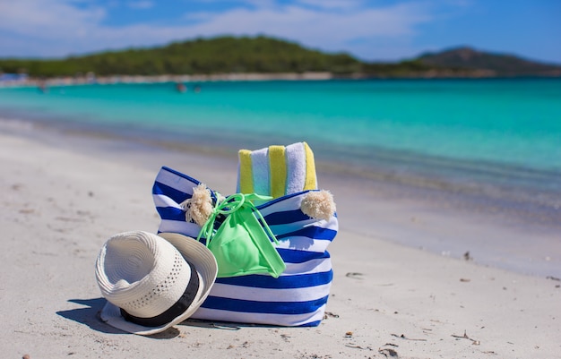 Borsa a strisce, cappello di paglia, crema solare e frisbee sulla spiaggia tropicale di sabbia bianca