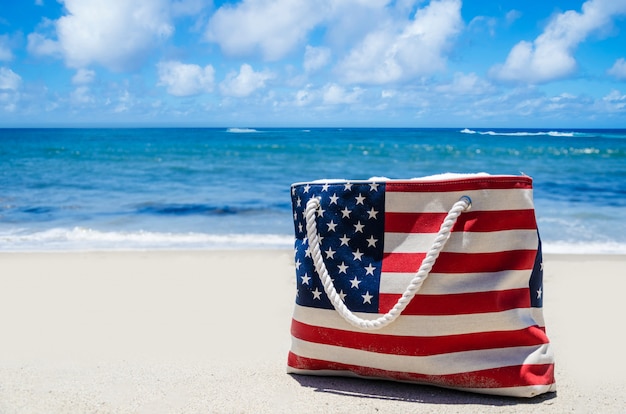 Borsa con i colori della bandiera americana vicino oceano sulla spiaggia di sabbia