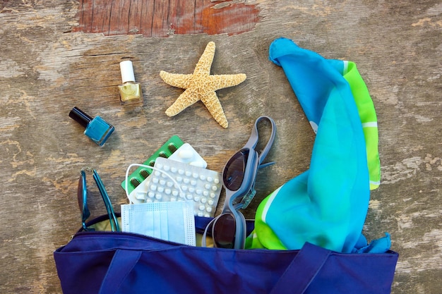 Borsa da spiaggia, accessori da donna, pillole e maschera medica protettiva su fondo di legno vecchio. Vista dall'alto.