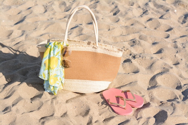 Borsa di paglia con occhiali da sole avvolgenti da spiaggia e infradito sulla sabbia Accessori estivi