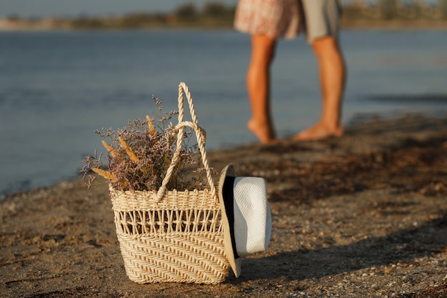 borsa di paglia con un mazzo di fiori sulla spiaggia al mare. sullo sfondo una silhouette di coppia. sfondo sfocato.