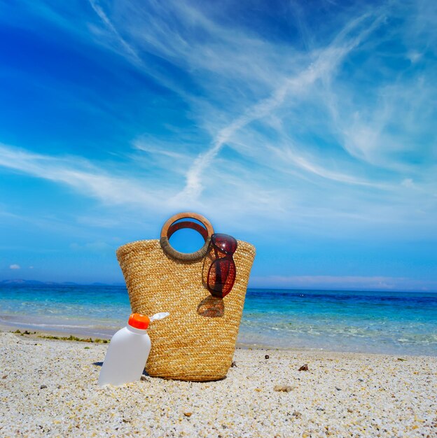 Borsa di paglia e bottiglia di crema solare sotto un cielo nuvoloso in riva al mare