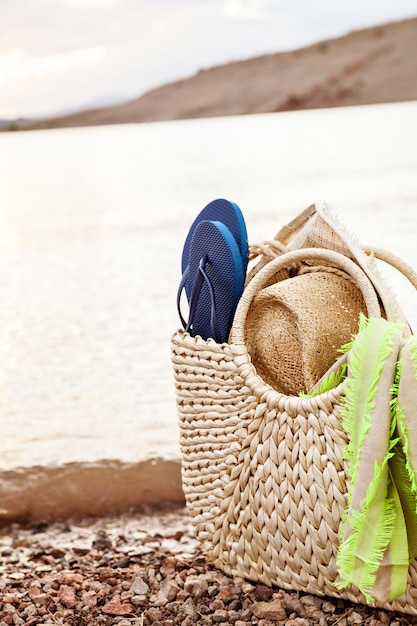 Borsa di paglia estiva e accessori da spiaggia sulla riva