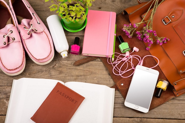 Borsa di paglia smart phone cuffie blocco note scarpe rosa passaporto e libro sulla scrivania di legno