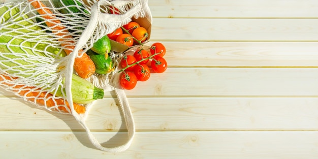 Borsa di stringa con verdure fresche Verdure fresche di fattoria in borsa a rete su fondo di legno rustico