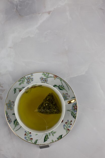 Borsa di tè verde con acqua in una tazza di porcellana su un piattino con una foto verticale con motivo floreale