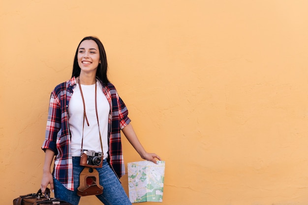 Borsa e mappa graziose felici della tenuta della giovane donna che stanno la parete vicina della pesca