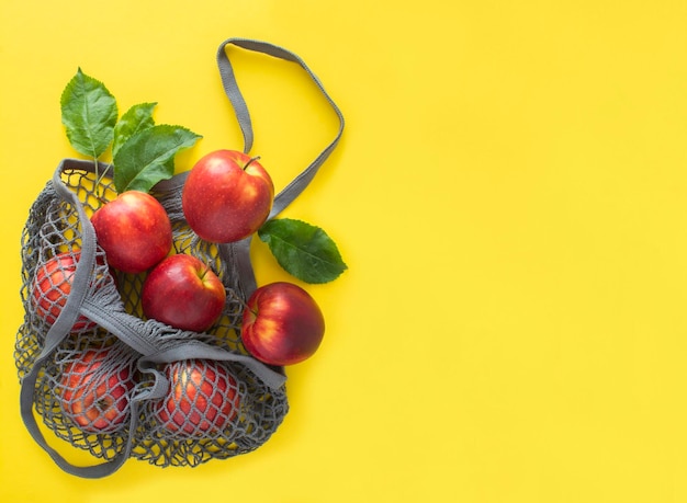 Borsa grigia per lo shopping in mesh con mele rosse su sfondo giallo Copia spazio Nessun concetto di sacchetto di plastica