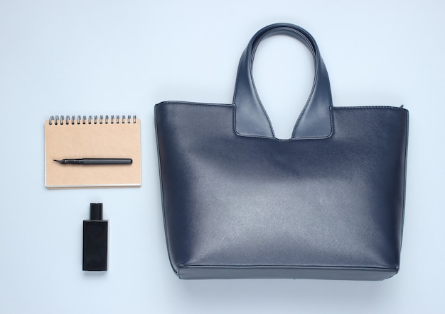 Borsa in pelle, quaderno, bottiglia di profumo su un tavolo grigio. Accessori business e moda. Vista dall'alto, minimalismo