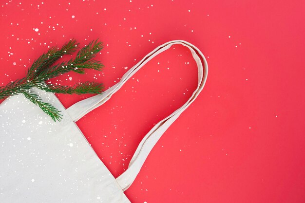 Borsa in tela di cotone bianco e ramo di albero di Natale sullo sfondo rosso brillante