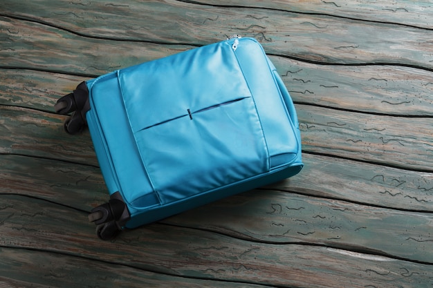 Borsa portabagagli blu su ruote. Valigia su fondo di legno verde. È ora di partire. Non dimenticare il tuo bagaglio.