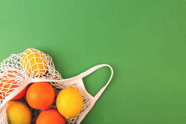 Borsa riutilizzabile della rete della frutta con le arance ed i limoni su fondo verde. Concetto di rifiuti zero. Disteso, copia spazio.