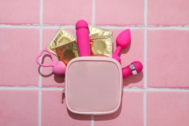 Borsa rosa con preservativi e giocattoli sessuali su sfondo rosa