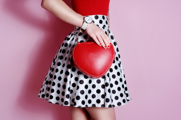 Borsa rossa a forma di cuore piccolo di moda in mano della ragazza. Gonna a pois bianca e nera