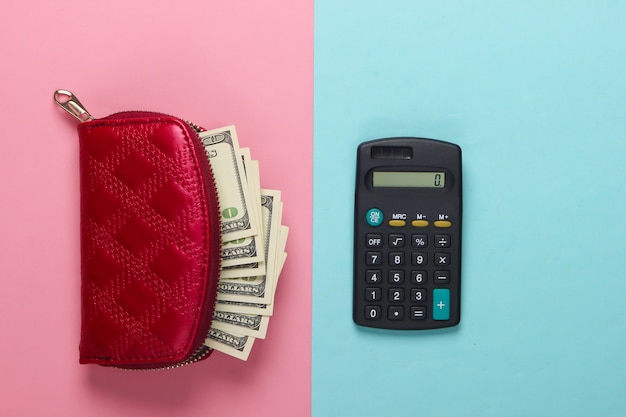 Borsa rossa con banconote da cento dollari e una calcolatrice su un pastello blu-rosa.