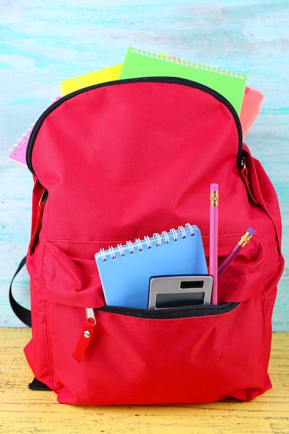 Borsa rossa con materiale scolastico su fondo di legno