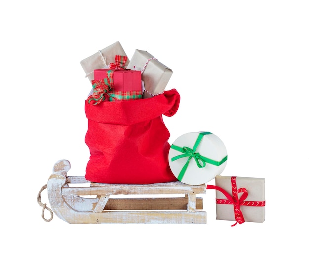 Borsa rossa di Babbo Natale con i regali di Natale su una slitta di legno isolata su bianco immagine stock