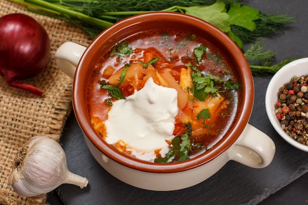 Borsch tradizionale ucraino con panna acida in ciotola di porcellana con pane di segale, prezzemolo, cipolla, aglio su tela di sacco e tavola di pietra. Vista dall'alto.