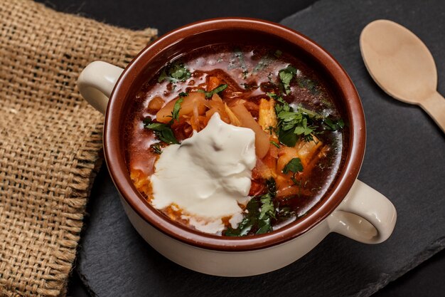 Borsch tradizionale ucraino con panna acida in una ciotola di porcellana con cucchiaio di legno su tavola di pietra. Vista dall'alto.