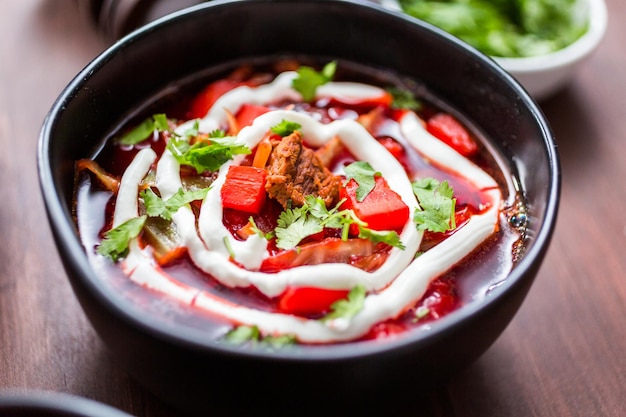 Borscht guarnito con panna acida e prezzemolo in una ciotola nera.