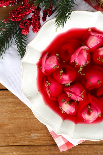 Borscht rosso chiaro polacco tradizionale con gnocchi e decorazioni natalizie sulla superficie del tavolo in legno