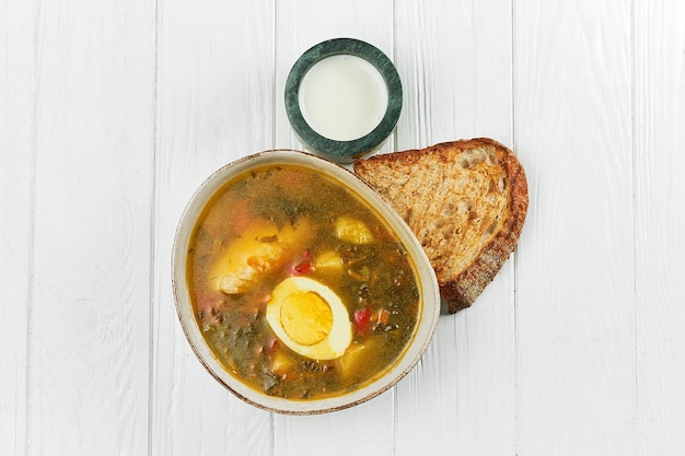 Borscht verde in un piatto su un fondo di legno bianco