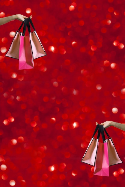Borse della spesa in mano femminile con scintillii di vacanza su sfondo rosso boke