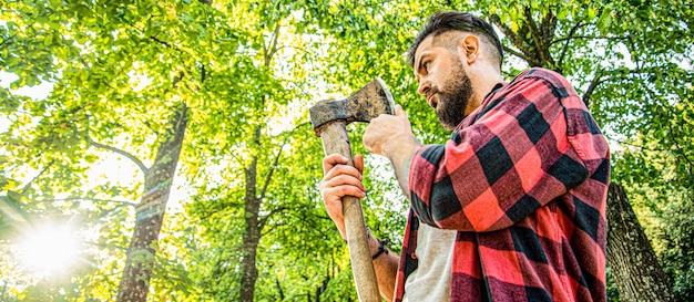 Boscaiolo con camicia a quadri tra gli alberi Boscaiole tagliando legna Brutale