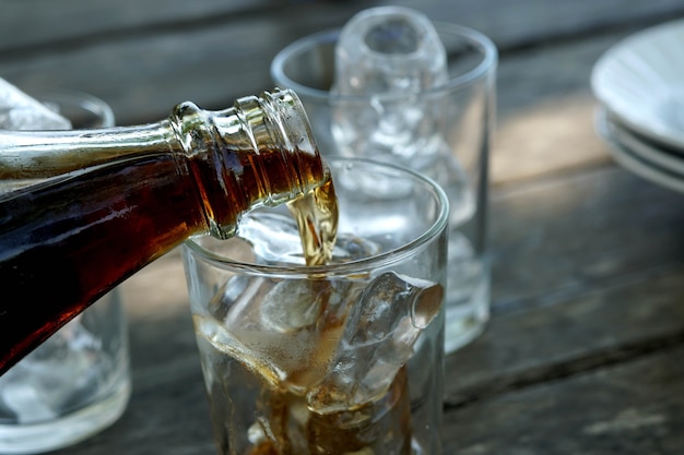 Bottiglia che versa acqua di cola per bere un bicchiere con ghiaccio in un caffè con terrazza