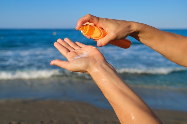 Bottiglia con crema solare nelle mani di una donna sulla spiaggia, sullo sfondo del cielo del mare. Creme protettive per la pelle con filtro spf, vacanze estive al mare