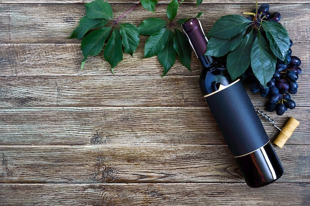 bottiglia con vino rosso cavatappi uva blu foglie su un tavolo di legno