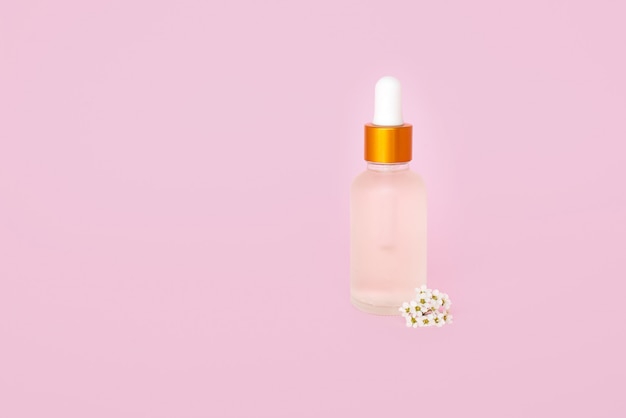 Bottiglia cosmetica in vetro con olio. contenitore per un prodotto per donna con piccoli fiori bianchi su sfondo turchese. Barattolo cosmetico. Posto per il testo