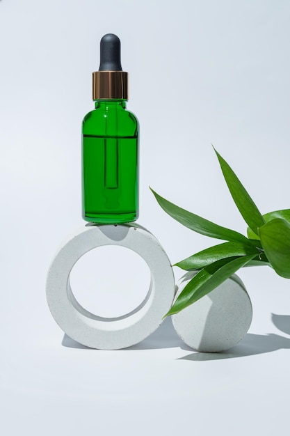 Bottiglia cosmetica in vetro ghiacciato con pipetta su podio rotondo bianco imballaggio del prodotto con ramo di rusco naturale siero anti-invecchiamento con peptidi cosmetici modello di concetto di spa