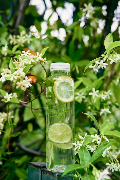 Bottiglia d'acqua con fettine di limone e lime all'interno si trova su un palo vicino a un albero in fiore