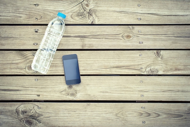 Bottiglia d&#39;acqua con il telefono su fondo di legno