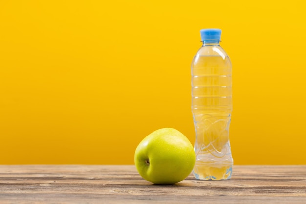 Bottiglia d'acqua con mela verde sulla tavola di legno