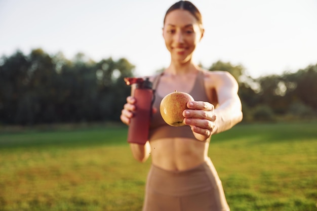 Bottiglia d'acqua e mela La giovane donna in abiti da yoga è all'aperto sul campo