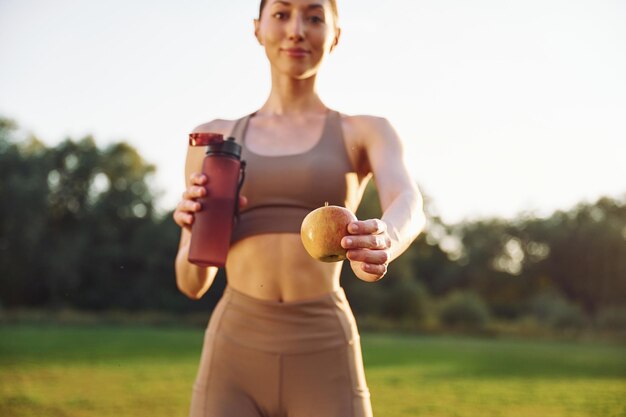 Bottiglia d'acqua e mela La giovane donna in abiti da yoga è all'aperto sul campo