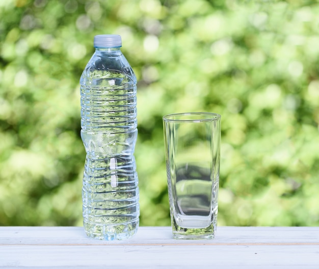 Bottiglia d'acqua e vetro sulla tavola di legno con natura verde