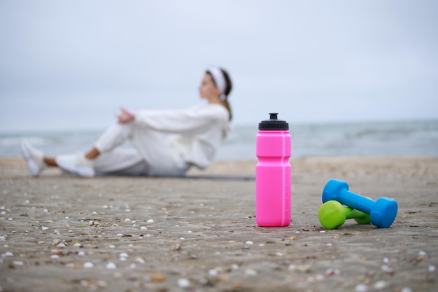 Bottiglia d'acqua rosa e manubri sulla sabbia Ragazza che fa i suoi esercizi in spiaggia Foto di alta qualità