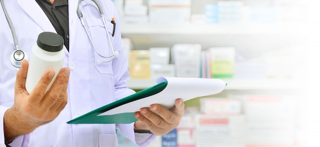 Bottiglia della medicina della tenuta del farmacista e compressa del computer per il riempimento della prescrizione nella farmacia della farmacia