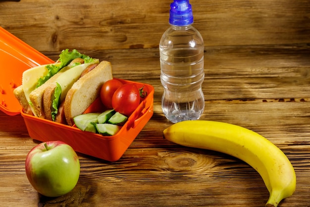 Bottiglia di acqua mela banana e pranzo al sacco con panini e verdure fresche su un tavolo di legno