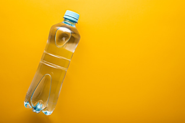 Bottiglia di acqua potabile pulita di plastica piccola blu di vista superiore con lo spazio della copia su colore giallo