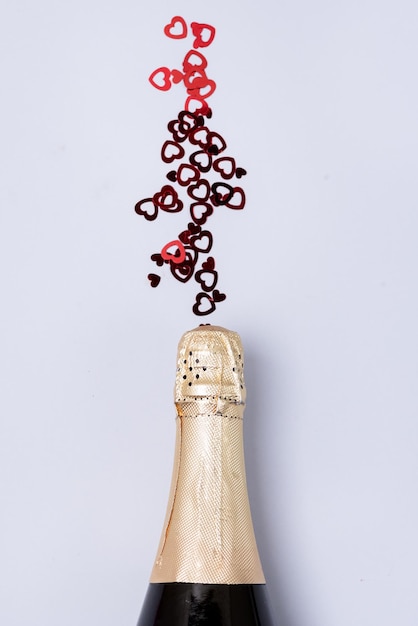 Bottiglia di Champagne con coriandoli a forma di cuori Sfondo blu Concetto di San Valentino