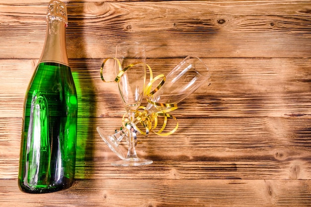 Bottiglia di champagne e due bicchieri da vino decorati con nastro dorato su tavola di legno Vista dall'alto