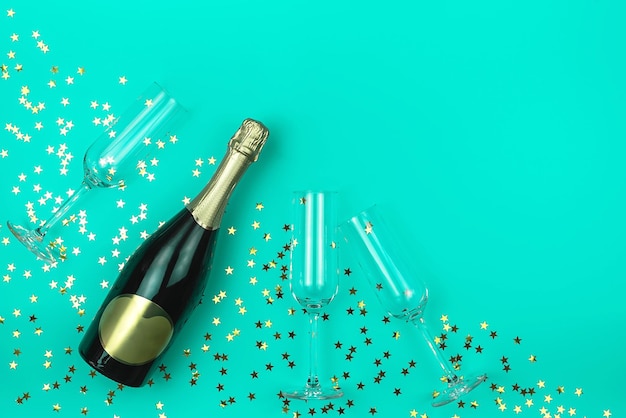 Bottiglia di champagne e tre bicchieri su sfondo di menta alla moda con confetti a forma di stella dorata Concetto di vacanza Mockup per il tuo design Stile piatto