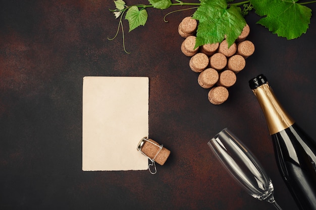 Bottiglia di champagne, gape grappolo di sughero con foglie, bicchiere di vino e carta su sfondo arrugginito.