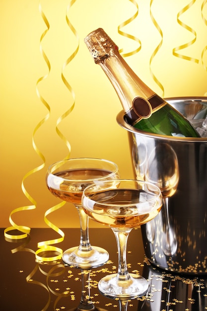 Bottiglia di champagne nel secchio con ghiaccio e bicchieri di champagne, su sfondo giallo