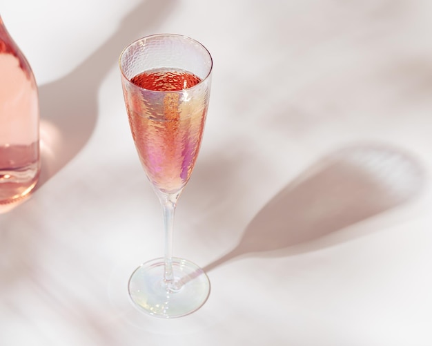 Bottiglia di champagne rosato spumante e bei bicchieri luminosi con luce solare sul tavolo luminoso