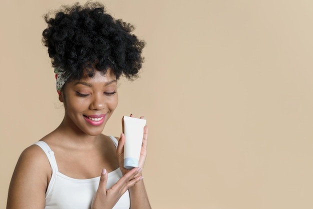 Bottiglia di crema cosmetica con un mockup nelle mani di un modello femminile afroamericano su sfondo beige Bella crema idratante per donna nera